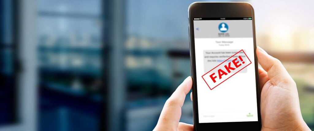 Hand holding a mobile phone with a scam text message appearing and a red banner saying "fake" displayed across the message