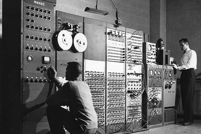 greyscale photo of 2 people looking at data servers