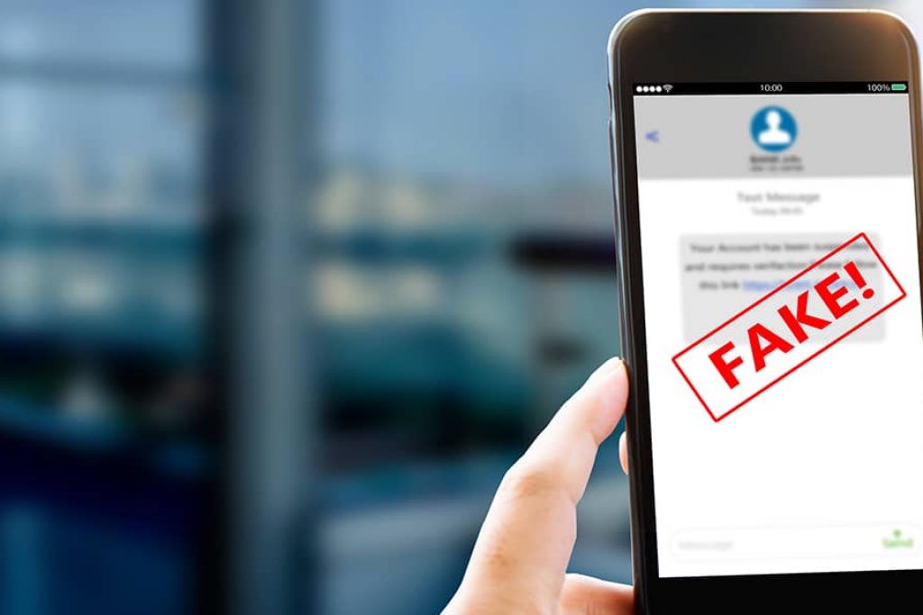 Hand holding a mobile phone with a scam text message appearing and a red banner saying "fake" displayed across the message